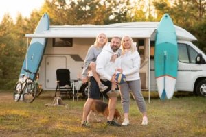 Happy parents with their child playing with a ball near their mobile home in the woods.