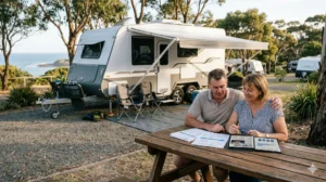 Couple reviewing caravan finance documents at a coastal campsite next to their RV.